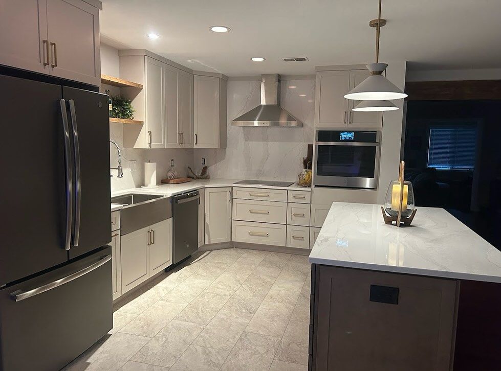 L-shaped kitchen with light gray shaker cabinets, quartz counters and a chimney range hood